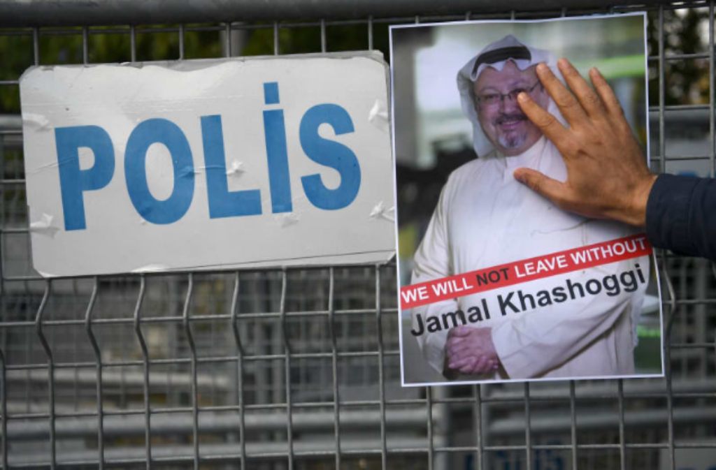 A Jamal Khashoggi poster held by a hand against a police fence.